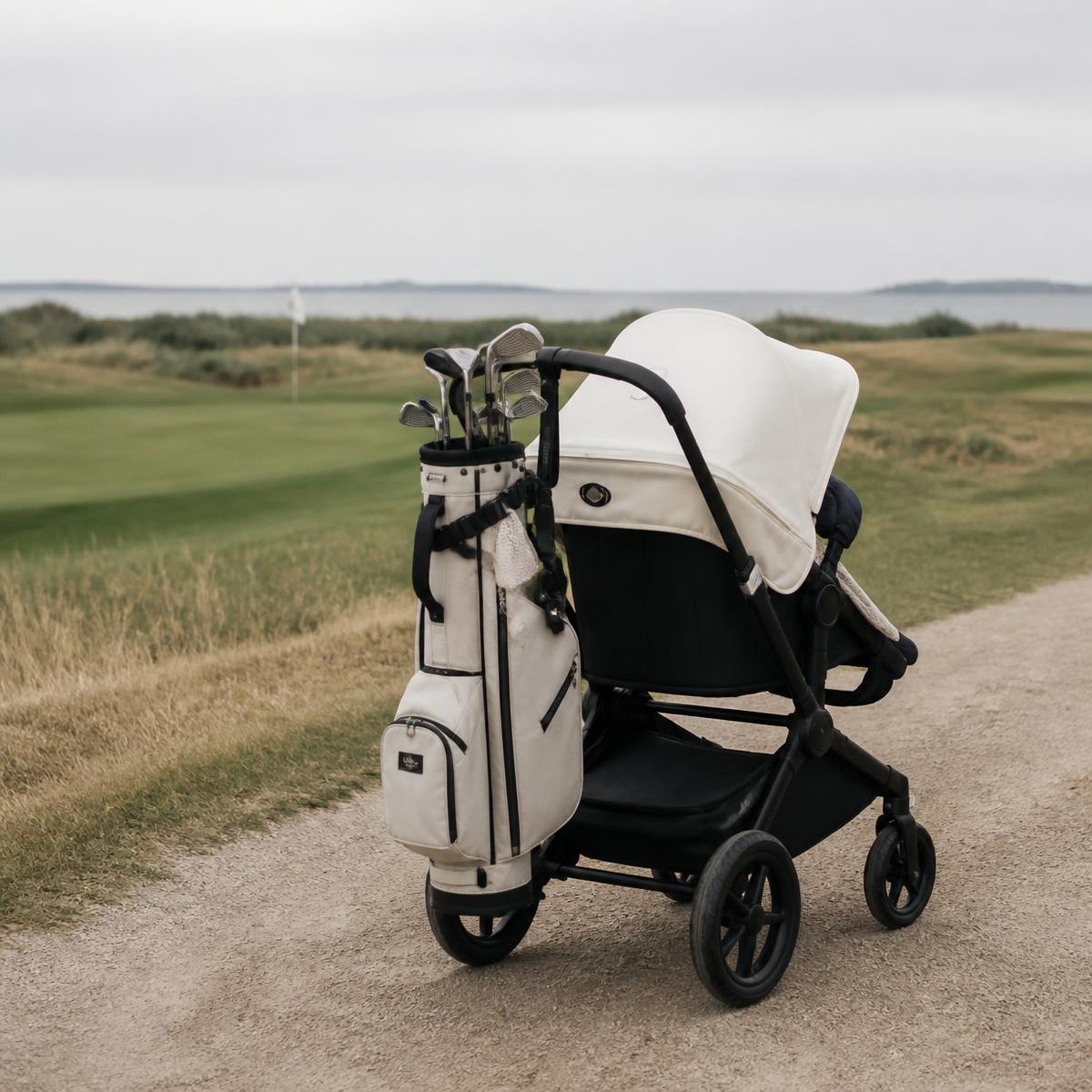 Barnvagn med golfbag hängande på sidan på en grusväg vid en golfbana